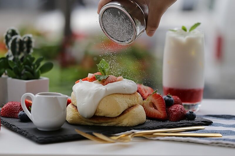 Japanese Fuwa Fuwa pancakes and sliced berries with someone shaking powdered sugar on top