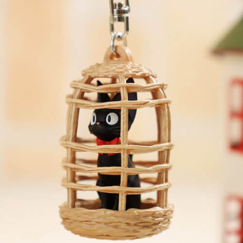 A keychain of Jiji from Kiki's Delivery Service sitting in a bird cage pretending to be a stuffed animal.