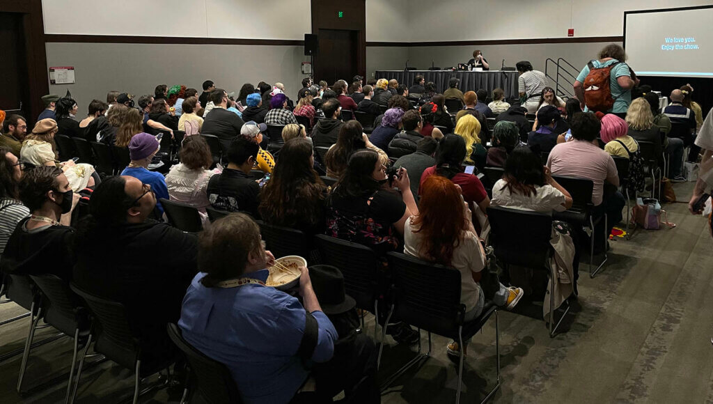 That 2008 Feeling: Exploring the Era of the 2000s Anime Bubble panel at Anime Boston 2023. An at capacity panel with Sam at the front of the room talking to the audience. The panel projector saying, "We love you. Enjoy the show."