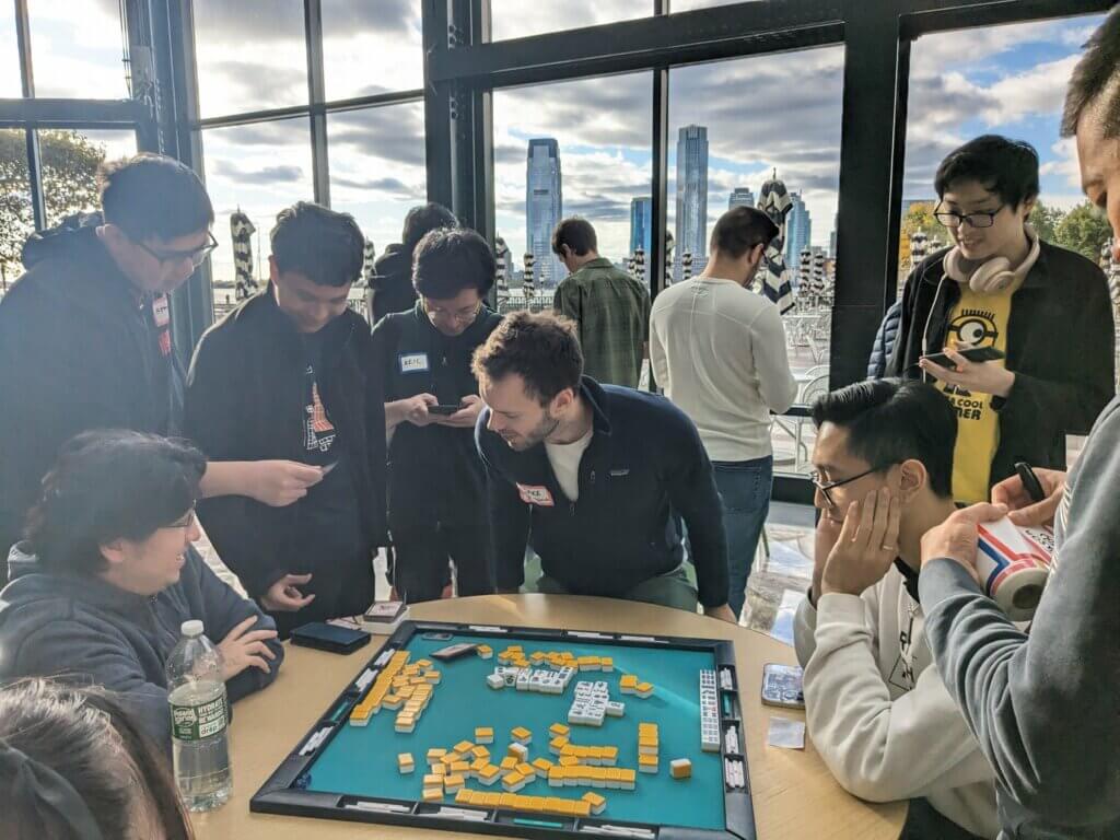 Mahjong players gathering around a game at a Riichi Nomi NYC meetup.