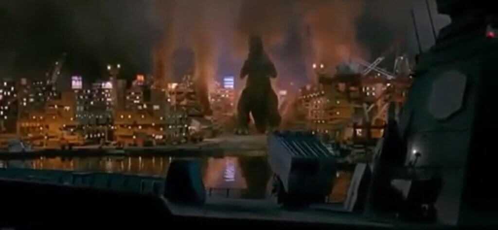 Godzilla stands in the ruins of Tokyo. Flames and smoke surrounding him.