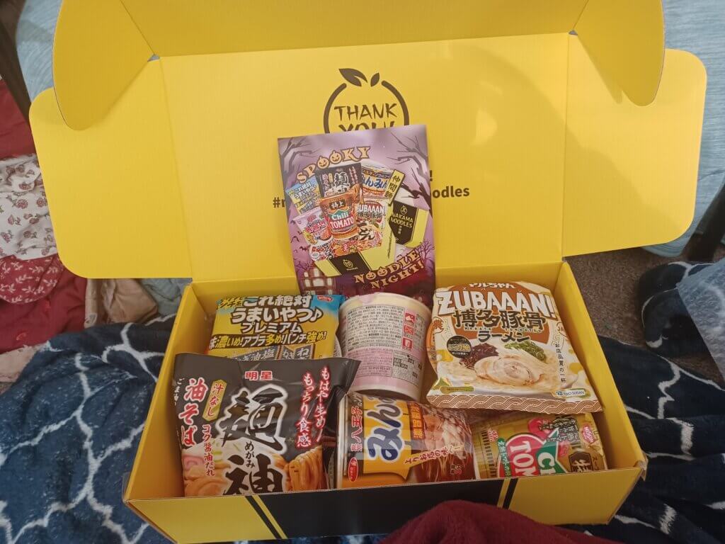 The eight containers of ramen within the sturdy yellow box.