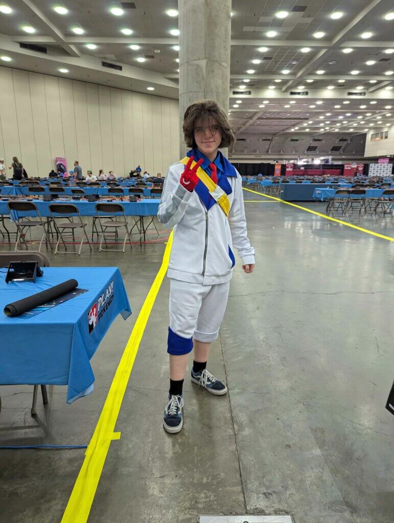 A player cosplaying as the character Kieran from the Scarlet/Violet DLC, wearing his white and blue school uniform.