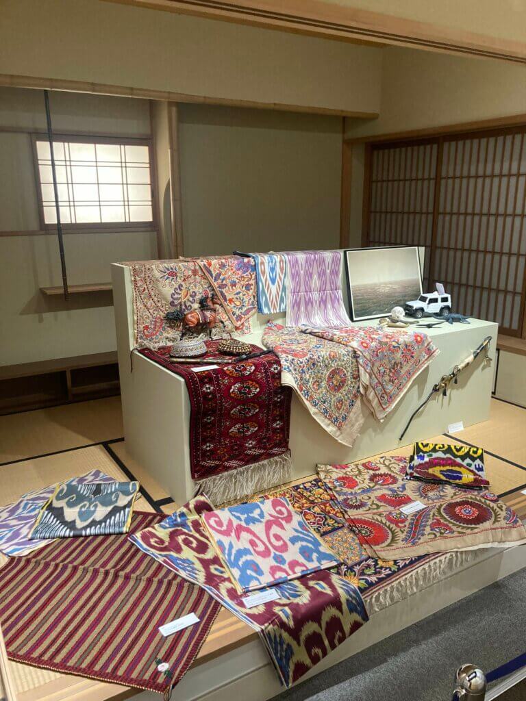 In a traditional Japanese room within the exhibit, several small carpets rest on a tatami mat and chair-shaped stand. 