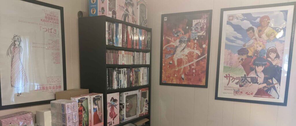A collection of Sakura Wars merchandise featuring posters on the walls and shelves filled with books, DVDs, games, and figures.