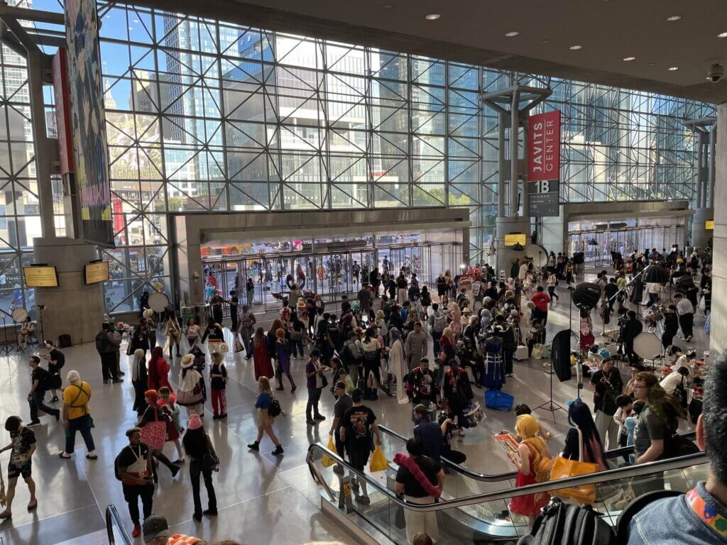 The entrance of the Javits Center. A crowd of people can be seen descending an escalator, including some in cosplay.