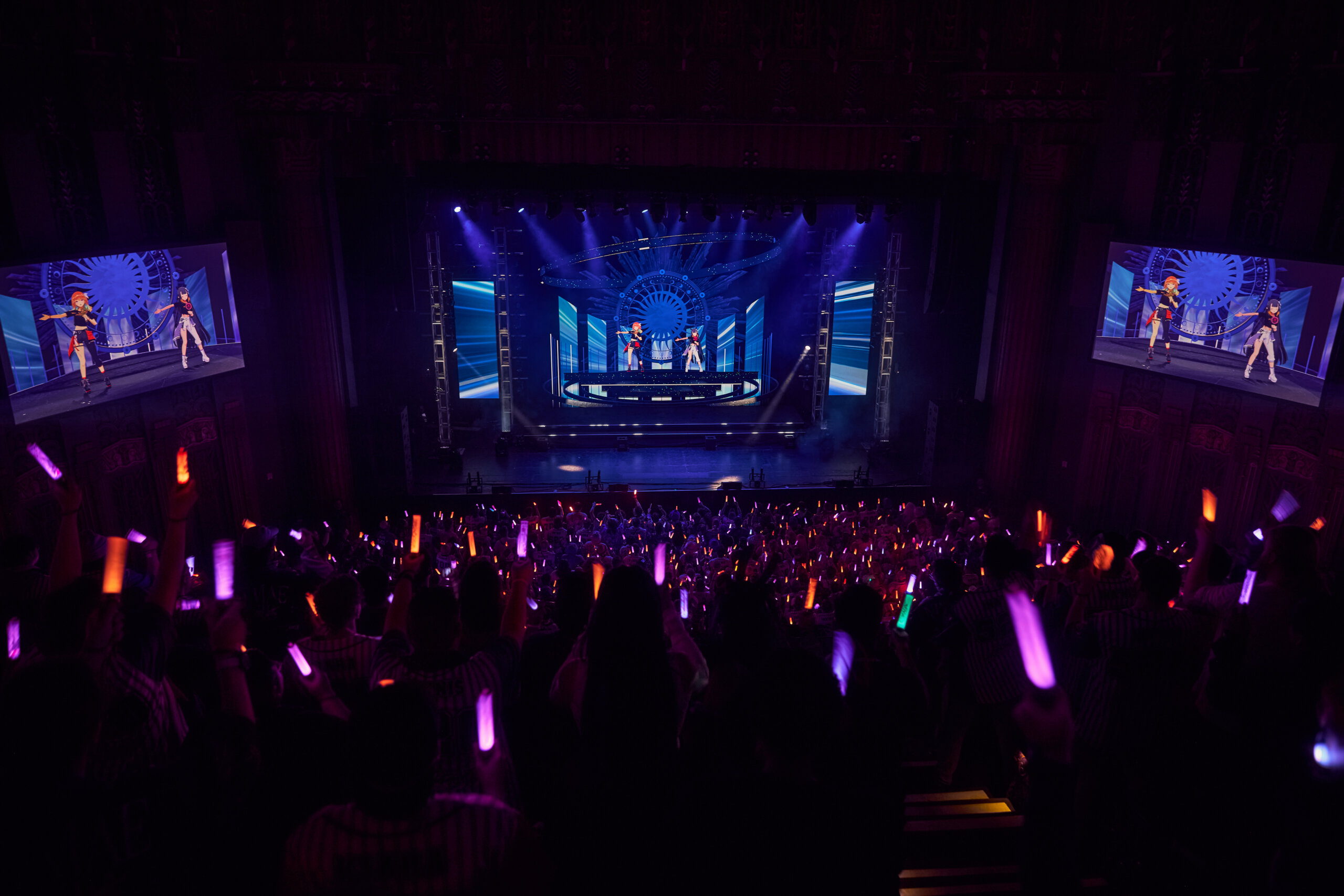 A balcony shot of Kiara and Ina performing together. The crowd has orange and purple light sticks. 