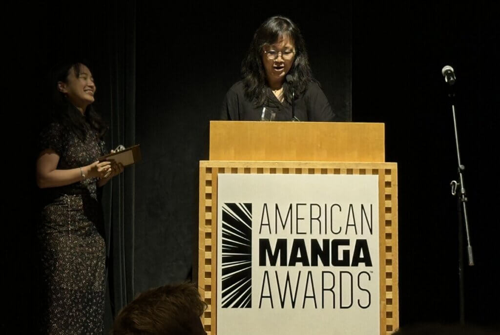 Wendy Chan, a woman wearing black, stands at a podium reading "American Manga Awards." Amanda Chung stands to her left.