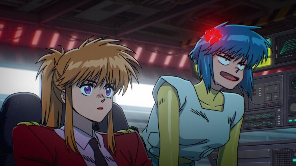 Motoko stands next to another woman who is typing at a keyboard. Motoko has an enraged expression on her face.
